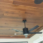 A black fan attached to a wooden ceiling